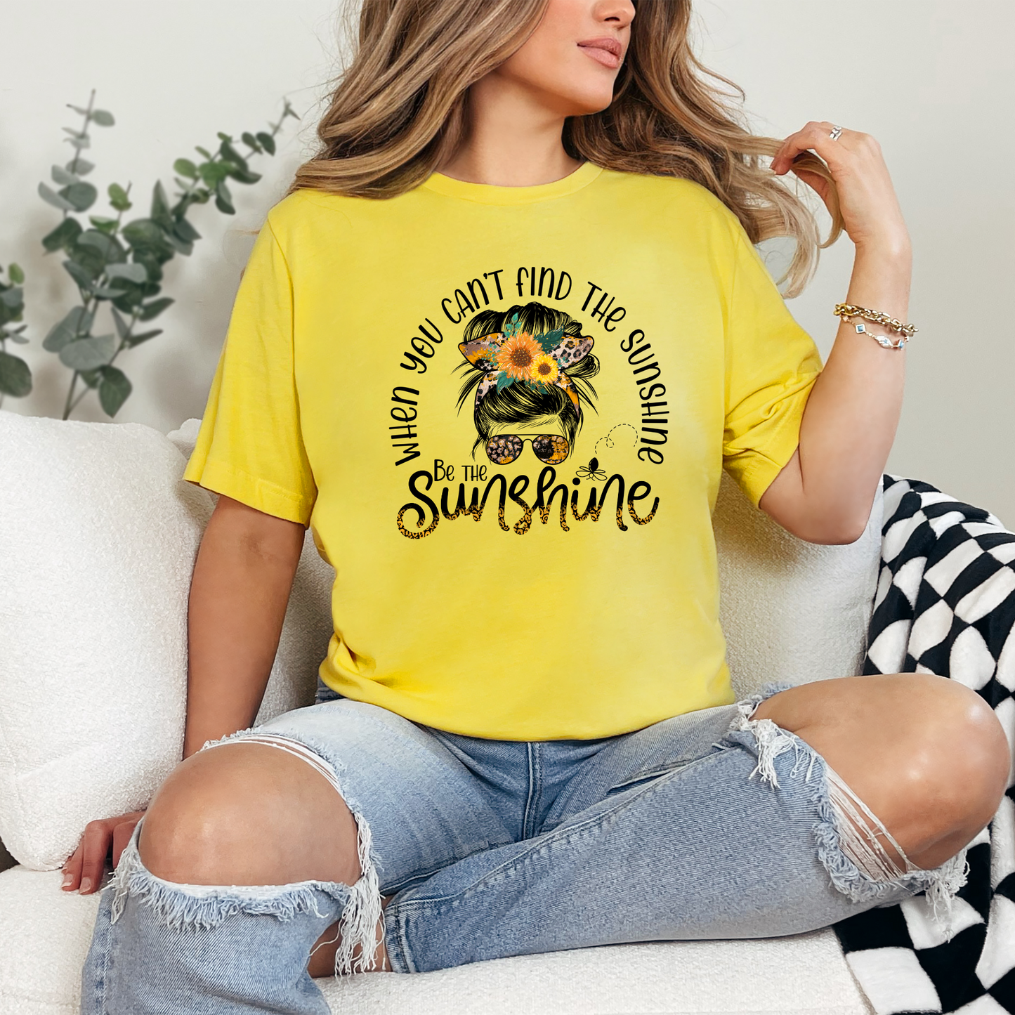 A person wearing a yellow graphic t-shirt with the text 'When you can't find the Sunshine' and a sunflower design.